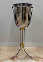 Front view of the assembled champagne cooler and stand showing stainless steel bucket and tubular stand with gold-tone accents.
