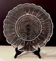 Clear sunflower art glass platter on a black stand, showing detailed center and petal texture