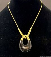 Front view of the gold-tone modernist TRIFARI necklace featuring the black resin teardrop-shaped pendant with knot design on a black display bust.