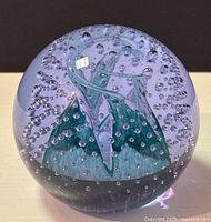 Clear glass spherical paperweight with purple and blue swirling design inside and embedded air bubbles, photographed from two angles revealing internal details and overall shape.