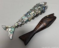 Both fish bottle openers side by side on a table showing size and details of abalone shell and wood carvings.