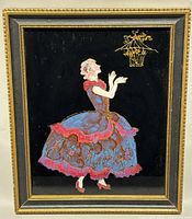 Full front view of framed vintage tinsel painting on black glass showing woman in Victorian dress and birdcage with birds in gold.