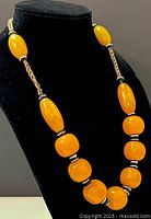 Necklace on a black bust, showing large yellow and orange beads with black and white separators on a braided cord