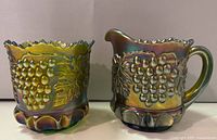 Both sugar bowl and creamer visible from front showing grape cluster and leaf embossing with iridescent finish.