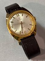 Front view of the Rodania vintage wristwatch showing gold-tone case, silver dial with gold-tone numeric and stick markers, black leather strap.