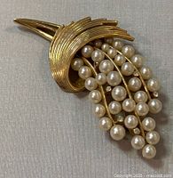 Front view of vintage Trifari brooch, showing gold-tone metal design with faux pearls and rhinestone accents.