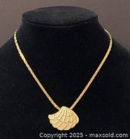 Front view of the gold-tone chain necklace with shell-shaped pendant displayed on a black bust.
