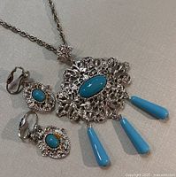 Set showing necklace with elongated oval blue cabochon pendant and three dangling blue teardrop cabochons, along with matching clip-on earrings featuring smaller blue cabochons.