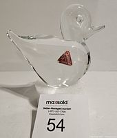 Clear Murano art glass duck figurine shown from side view with original red triangular Murano glass sticker visible on body.