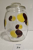 Front side view of clear glass cookie jar with yellow and brown painted abstract designs and lid