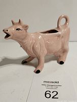 Front side view of a light pink ceramic cow creamer with details of black accents on the hooves and eyes, and an open mouth for pouring.