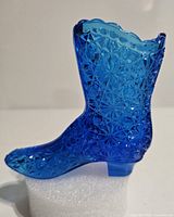 Side view of the vintage blue glass boot showing detailed daisy and starburst pattern with scalloped top edge and small heel.