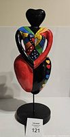 Front view of colorful stylized paper mache sculpture of a woman holding a heart.