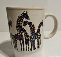 Side view of the white ceramic mug showing colorful stylized giraffe designs in orange, pink, blue, and purple with a gold rim line on top.