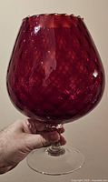 Hand holding a large deep red Empoli Italian art glass goblet with textured pattern, clear stem and round base.