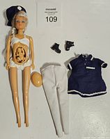 Simba Toys Steffi doll with open belly showing articulated child figure, lying alongside white leggings, navy blue dress, hat and black shoes.