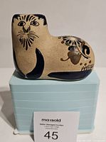 Front view of the vintage Tonala cat pottery figurine placed on a light blue box with maxsold lot number.