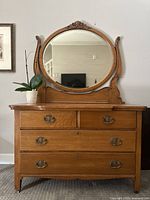 Full front view of antique Victorian oak dresser with four drawers and attached oval mirror, showing wood grain and decorative brass handles.