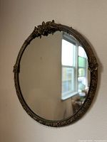 Side angle photo of large round antique mirror hanging on wall showing intricate floral carved frame.