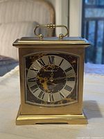 Front view of the brass carriage mantle clock showing face with Roman numerals and mottled background.
