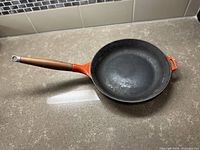 Full view of vintage Le Creuset Alpine Wood Handle Fry Pan with flame orange exterior and black interior on countertop.