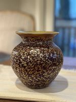 Photo of Lundberg Studios handmade glass vase showing brown and gold speckled pattern and flared rim on a light surface with indoor background.