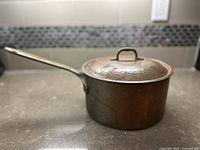 Side view of vintage copper pot with attached handle and lid, showing hammered texture and aged finish.