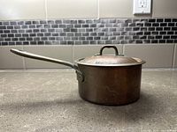 Side view showing the copper pot and long metal handle with lid on top.
