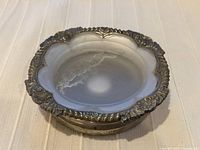 Top view of vintage silver plate wine coaster showing ornate shell pattern on rim and glass insert inside.