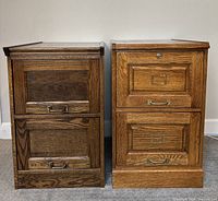 Two vintage solid wood file cabinets side by side, lighter wood finish, showing front view with two drawers each with metal handles and label holders.