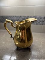 Side view of vintage Towle silverplate pitcher showing ornate handle and claw feet on countertop