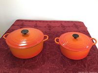 Both Le Creuset Dutch ovens side by side showing sizes and vibrant orange color.