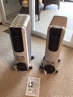 Two standing radiant heaters on carpet, showing front control panels and paper manual.