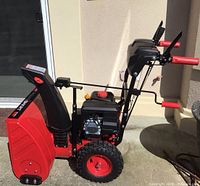 Side view of the entire red PowerSmart snow thrower showing large tires, handlebar with controls, and snow chute.