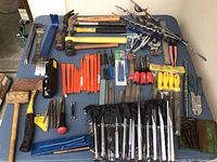 Full overview of table showing assorted hammers, mallets, pry bars, chisels, punches, screwdrivers, files and auger bits.