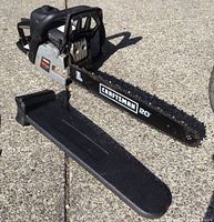 Photo of the Craftsman gas chainsaw with 20-inch bar and protective black plastic cover lying on the ground.