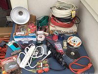 Photo showing various electrical supplies including coils of wire, extension cords, power strips, metal light fixture, and packaged wire connectors.
