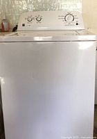 Front view of the white Kenmore Series 100 top-load washing machine showing its control panel and dent on the corner.
