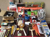 Full view of all painting supplies laid out on a surface including brushes, rollers, drop cloths, tape, scrapers, and cutting blades.