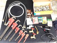 Full overview of all plumbing tools and fittings on black surface including pipe wrenches, valves, hoses, and seals.