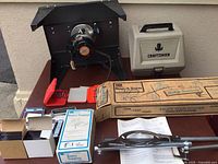 Full view of the Craftsman router mounted on the table with rust on the tabletop, plastic Craftsman tool case, boxed Mount-A-Form template, and various small tool kits and manuals on the table.