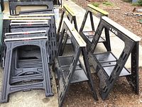 Three assembled sawhorses with black plastic legs and yellow top rails, piles of disassembled leg panels behind