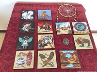 Overview of all 12 Southwestern hand painted ceramic tiles arranged on red fabric with dreamcatcher and cast metal brooch in the center.