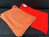 Stack of orange floral Calvin Klein placemats beside red hand-woven Madawaska placemats