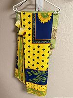Yellow, blue, green sunflower motif tablecloth hanging, partial view of green wine-label cloth behind