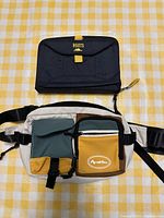 Roots black bagnote book and multicolor Apasttec bum bag laid flat on a yellow checkered cloth.