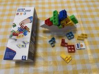 Photo showing boxed Tetris Pile Up Tower game and plastic Tetris shaped blocks arranged on table with balance stand.