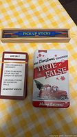 Photo of Pick-Up Sticks wooden box with sticks and Christmas True or False card game with festive cards and quiz question card