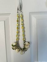 Photo showing the yellow bead and shell necklace hung on a white door to display the length and beads details.