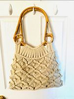 Front view of the beige crochet bag showing the woven texture and bamboo circular handles hanging on a door hook.